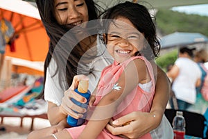 A happy daughter amused look at the camera when his mother give a sunblock