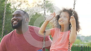 Happy daughter and daddy swinging in yard and waving hands to mom, family