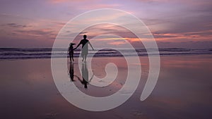 Happy daughter holding hands of dad on the beach running on sandy shore at sunset Amazing light sunset or sunrise sky watching tro