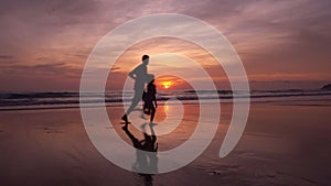 Happy daughter holding hands of dad on the beach running on sandy shore at sunset amazing light sunset or sunrise sky watching tro