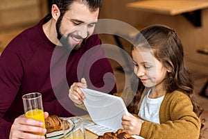 happy daughter looking at tablet while sitting with father