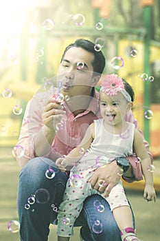 Happy daughter plays soap bubbles with father