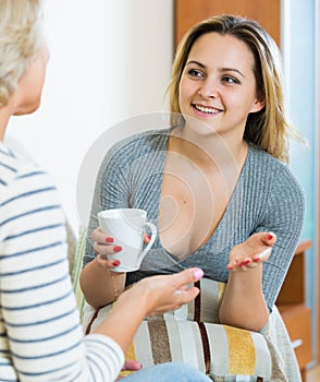 Happy daughter sharing gossips with mature mom while tea-drinking