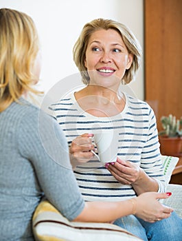 Happy daughter sharing gossips with mature mom while tea-drinking