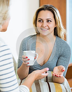 Happy daughter sharing gossips with mature mom while tea-drinking