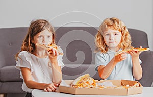 Happy daughter and son eating pizza. Children kids enjoy and having fun with lunch together at home. Little friends, boy