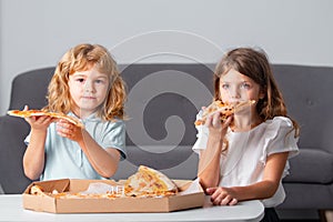 Happy daughter and son eating pizza. Children kids enjoy and having fun with lunch together at home. Little friends, boy