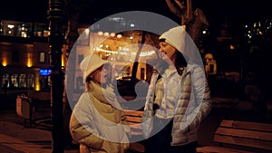 Happy daughter talking with mother on evening city street. Cheerful mom and teen daughter laughing on evening urban walk