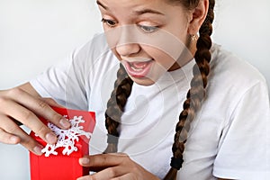 happy, delighted teenage girl with long braids opens beautiful gift box and looks inside. Congratulations on holiday