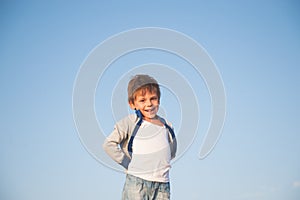 Happy delightful smiling little boy in sweater on blue sky background