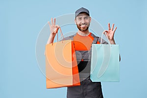 Happy delivery man in uniform holding shopping bags on blue studio background