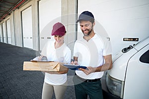 Happy delivery man and woman writing on clipboard next to van