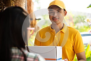Happy delivery man in yellow polo shirt uniform with parcel post box in hands standing in front of customer`s house doors. Smilin