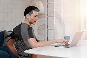 Happy disabled Asian man sitting in a wheelchair And working with computer at home, The concept of Technologies for the