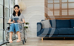 Happy disabled Asian woman sitting in a wheelchair And working with tablet at home, The concept of Technologies for the