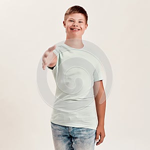 Happy disabled boy with Down syndrome smiling and reaching out his hand towards camera while posing isolated over white
