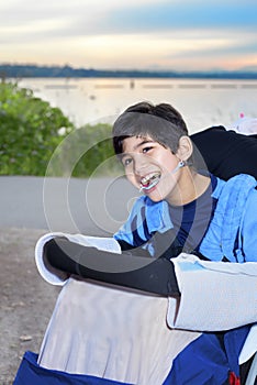 Happy disabled boy in wheelchair by lake at dusk