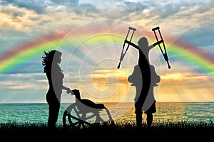 Happy disabled child on the father shoulders holding crutches nurse and wheelchair rainbow sea