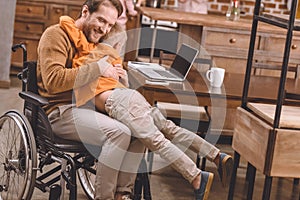 happy disabled father in wheelchair hugging with cute little son