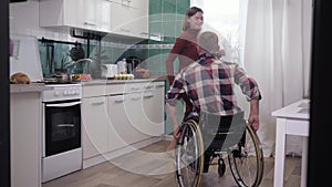 Happy disabled man in a wheelchair is having fun dancing with his girlfriend in kitchen while cooking