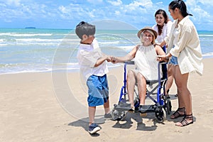 Happy disabled senior elderly woman in wheelchair spending time together with her family on tropical beach. Asian grandma,