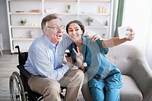 Happy disabled senior man taking selfie with lovely young doctor at home