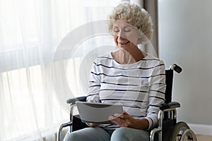 Happy disabled senior woman sit on wheelchair using digital tablet