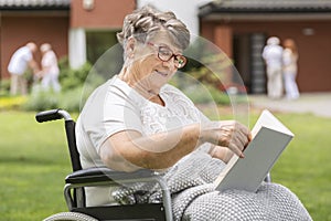 Happy disabled senior woman in a wheelchair reading book