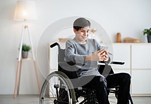 Happy disabled teen in wheelchair using digital tablet at home, browsing internet or watching videos, copy space