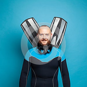 Happy diver diving man with flippers smiling against bright blue studio wall background