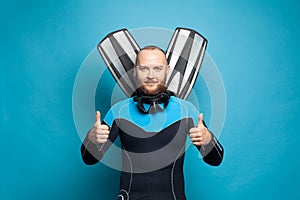 Happy diver with fins showing thumb up gesture on blue background