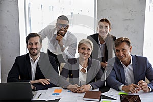 Happy diverse business team sitting, standing at meeting table