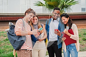 Happy diverse classmates looking at their smartphones and laughing together watching funny videos after class. Young