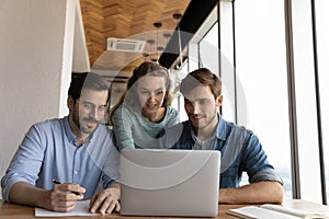 Happy diverse colleagues brainstorm using laptop in office