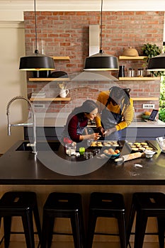 Happy diverse couple in aprons decorating christmas cookies in kitchen, copy space