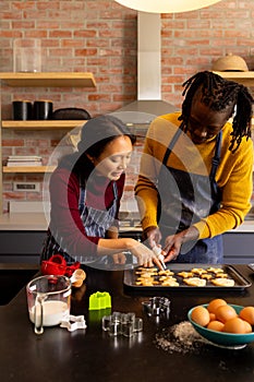 Happy diverse couple in aprons decorating christmas cookies in kitchen, copy space