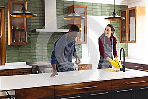 Happy diverse couple cleaning countertop and doing dishes in kitchen at home
