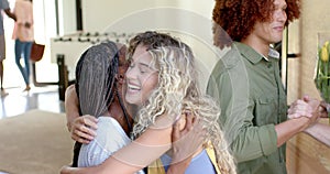 Happy diverse couple embracing and greeting friends at front door of home, slow motion