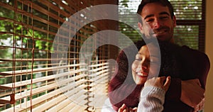 Happy diverse couple embracing and smiling in living room, looking to camera