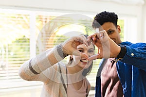 Happy diverse couple making a heart symbol with hands at home, copy space