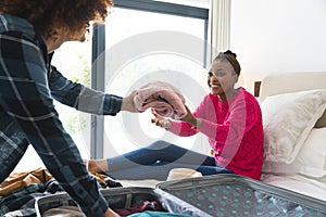 Happy diverse couple packing suitcase together in sunny bedroom, at home