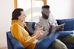Happy diverse couple sitting on sofa using tablet for online shopping at home