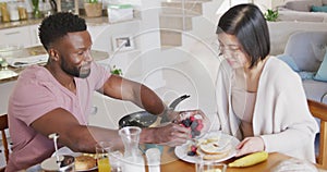 Happy diverse couple sitting at table and having breakfast