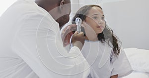 Happy diverse doctor examining sick girl patient with otoscopy in hospital in slow motion