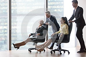 Happy diverse employees having fun riding on chairs in office