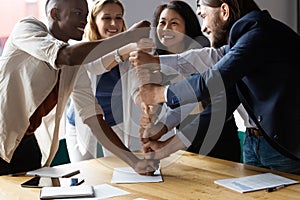 Happy diverse employees stack fists at corporate meeting, celebrating success