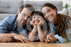 Happy diverse family lying on warm floor looking at camera
