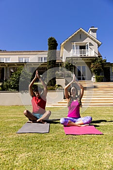 Happy diverse fit couple practicing yoga meditation sitting in sunny garden, with copy space