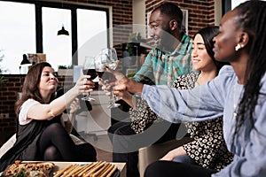 Happy diverse friends clinking wineglasses at birthday party in living room