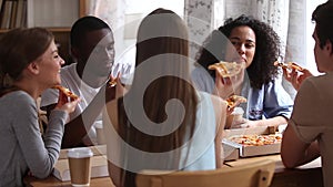 Happy diverse friends eating pizza drinking coffee share dinner meal